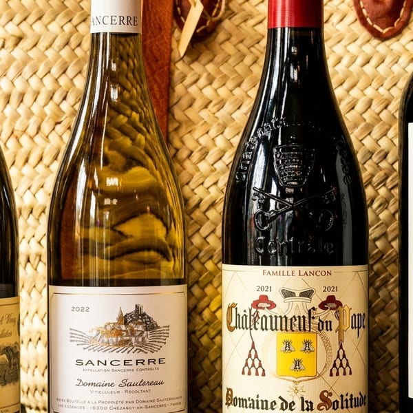 Four bottles of wine, two white and two red, standing against a woven basket.