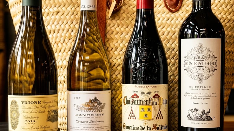 Four bottles of wine, two white and two red, standing against a woven basket.