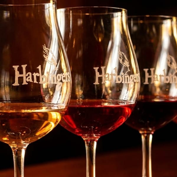 A row of wine glasses filled with red, rosé, and white wine, branded "Harbingers".
