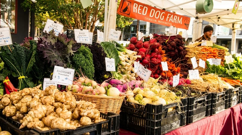 A vibrant farmers market stall from Red Dog Farm, overflowing with fresh root vegetables and leafy greens.