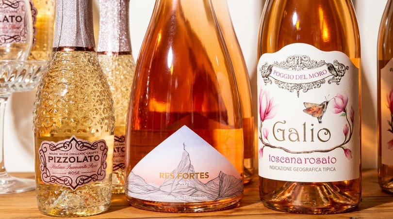 Several bottles of sparkling rosé wine, some with textured glass and decorative labels, on a wooden surface.