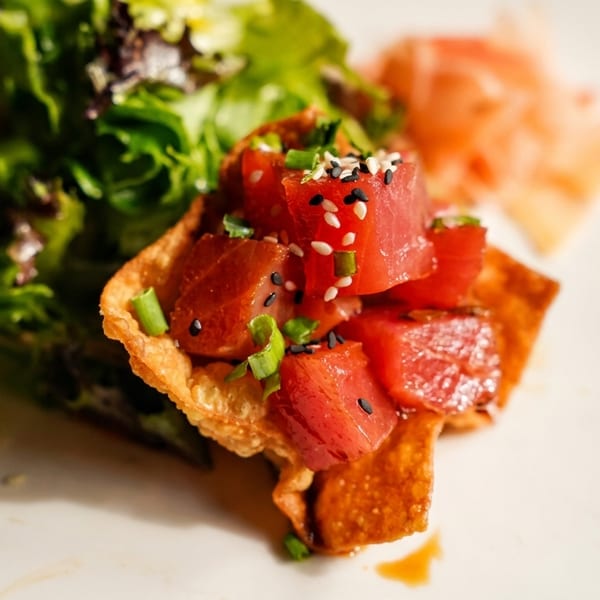 Close-up of tuna poke in a crispy wonton cup with green salad and pickled ginger.