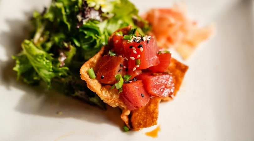 Close-up of tuna poke in a crispy wonton cup with green salad and pickled ginger.