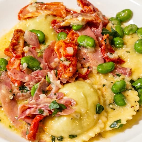 Ravioli dish with prosciutto, sun-dried tomatoes, and edamame in a light sauce.