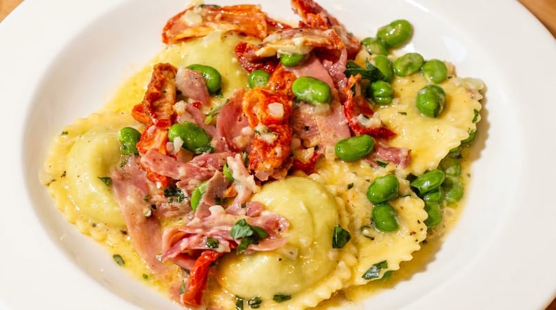 Ravioli dish with prosciutto, sun-dried tomatoes, and edamame in a light sauce.