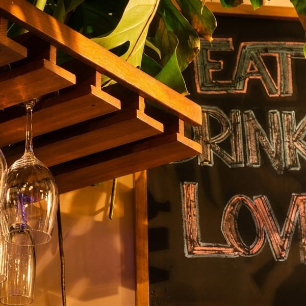 Wine glasses hang from a wooden rack next to a chalkboard sign that reads "EAT DRINK LOVE".