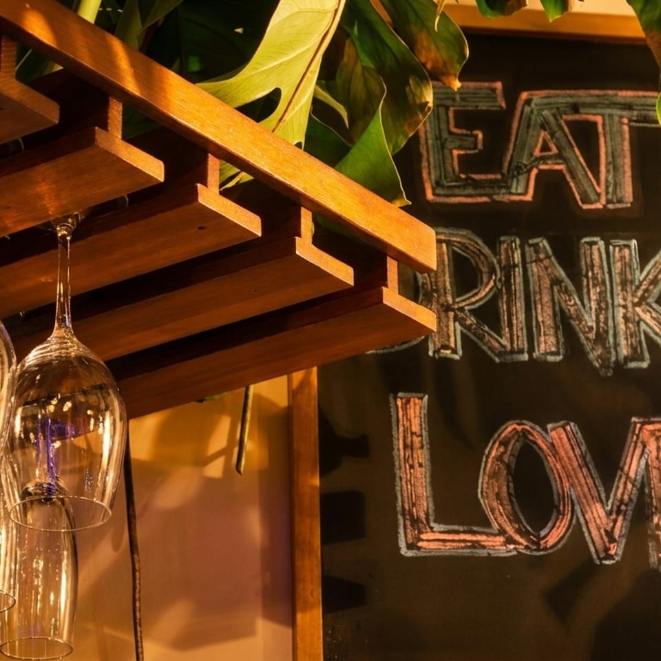 Wine glasses hang from a wooden rack next to a chalkboard sign that reads "EAT DRINK LOVE".