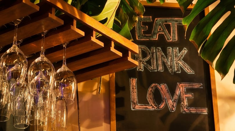 Wine glasses hang from a wooden rack next to a chalkboard sign that reads "EAT DRINK LOVE".